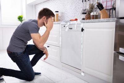 upset man sitting in front of damaged dishwasher